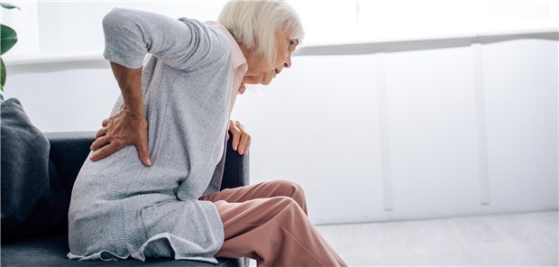 Seitenansicht einer älteren Frau mit Rückenschmerzen in ihrer Wohnung.