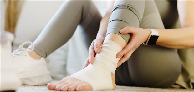 Eine Frau hält mit beiden Händen ihren schmerzenden verstauchten Knöchel.