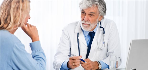 Eine Frau sitzt einem älterem Arzt gegenüber.