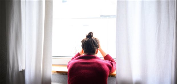 Eine Frau sitzt mit Kopf in den Händen am Fenster.