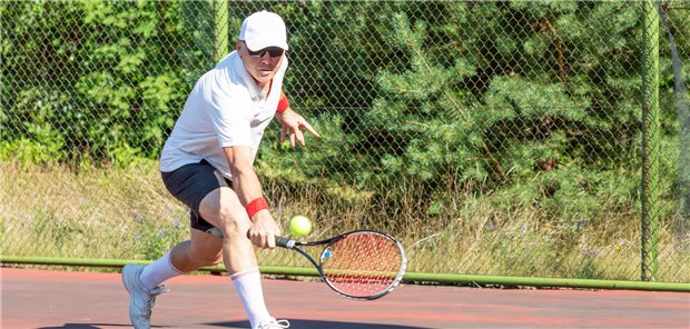 Ein älterer Mann spielt Tennis auf einem Platz im Freien.