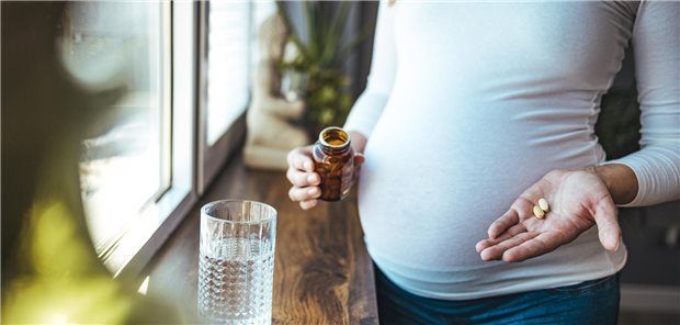 Eine schwangere Frau, die Tabletten mit einem Glas Wasser einnimmt.