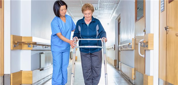 Eine Pflegekraft begleitet eine Frau, die einen Rollator schiebt.