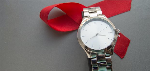 Eine Uhr vor einer roten Aids-Schleife