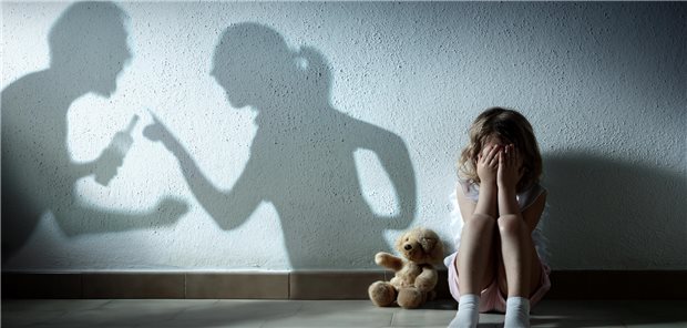 Ein kleines Mädchen sitzt weinend auf dem Boden. Hinter ihr sieht man die Schatten ihrer streitenden Eltern.