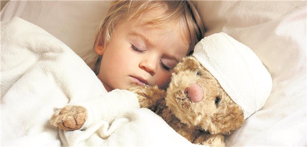 Ein Kind schläft mit seinem Teddy im Bett. Der teddy hat eine Bandage auf dem Kopf.