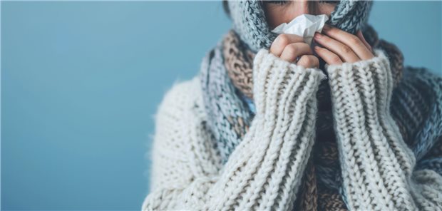 Frau in gestrickter Kleidung hält sich ein Taschentuch vor die Nase.