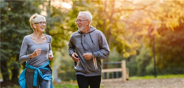 Eine ältere Frau und ein älterer Mann joggen im Park bei Sonnenuntergang. 