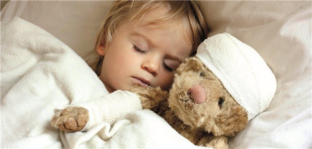 Kind liegt schlafend mit seinem Teddy im Bett.