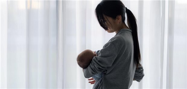 Frau kümmert sich um neugeborenes Baby hinter weißem Vorhang