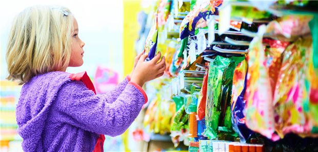 Blondes Mädchen vor Süßigkeiten auf Regalen im Supermarkt