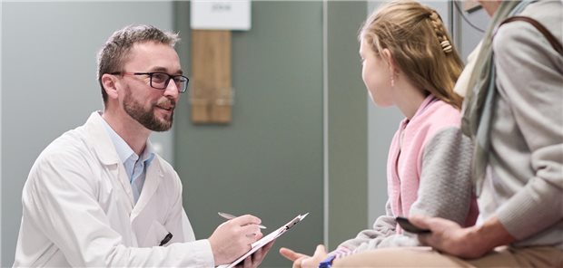 Ein Arzt geht neben einem Kind in die Hocke um mit ihm auf Augenhöhe zu sein. 