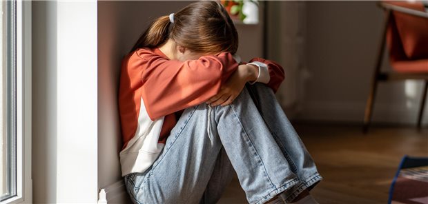 Mädchen sitzt auf dem Boden und verdeckt ihr Gesicht. 