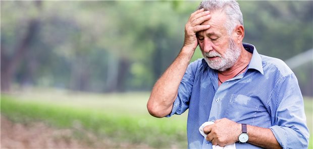 Mann mit grauen Haaren und Bart schwitzt stark und fasst sich an die Stirn. In einer Hand hat er auch ein Schweißtuch, im Hintergrund kann man Bäume und einen Rasen undeutlich erkennen.
