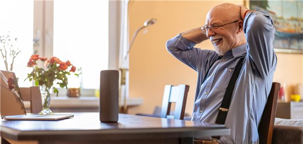Ein älterer Mann sitzt an einem Esstisch, vor ihm steht ein Alexa-Gerät