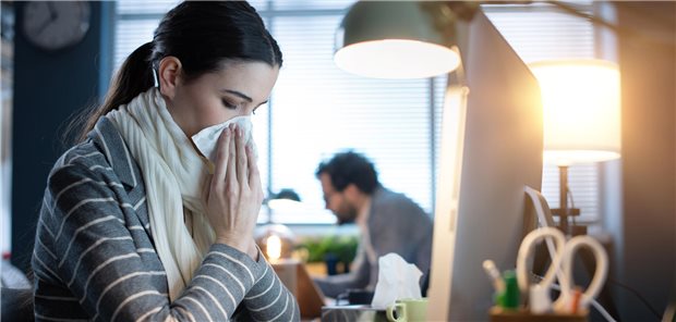 Eine Frau sitzt vor dem PC und schneuzt in ein Taschentuch.