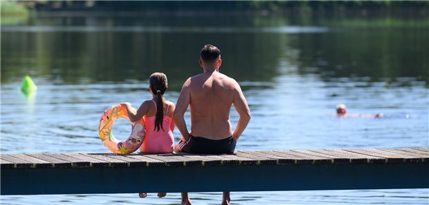 Ein Vater und seine Tochter sitzen am Steg eines Badesees