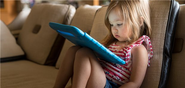 Ein junges Mädchen sitzt auf dem Sofa und benutzt ein Tablet.