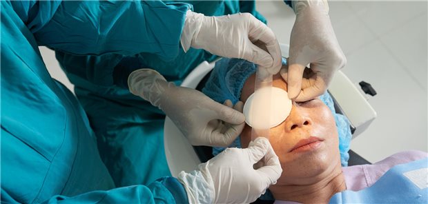 Zwei Chirurgen befestigen nach einer Operation ein Pflaster mit Klebeband auf dem Auge einer älteren asiatischen Patientin.