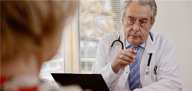 Ein Arzt, gekleidet in Hemd, Krawatte und Kittel, spricht mit einer Patientin.