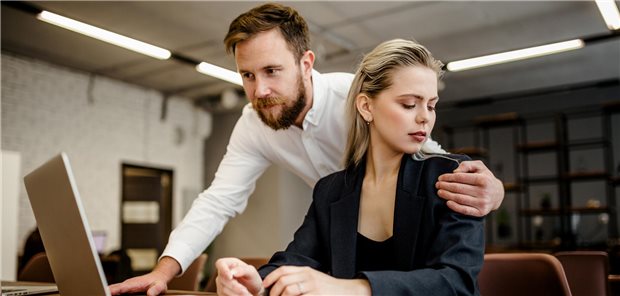 Mann fasst Frau an die Schulter, während er etwas an ihrem Computer macht.