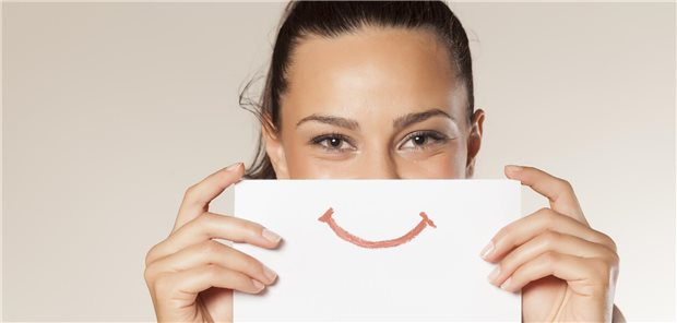 Nach der Corona-Pandemie: So zufrieden sind die Deutschen mit ihrer Gesundheit Frau mit Schild vor dem Gesicht, auf dem ein Smiley abgebildet ist.