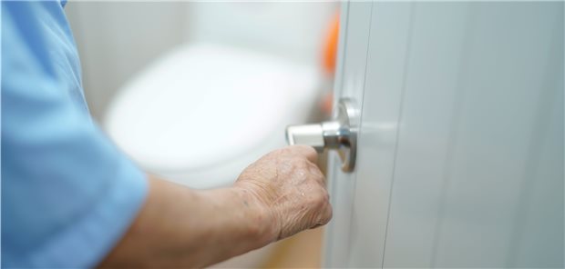 Ältere Person öffnet Tür zur Toilette (leicht verschwommen im Hintergrund, Symbolbild).
