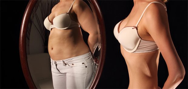 Eine schlanke Frau sieht sich selbst im Spiegel und sieht einen dicken Bauch.