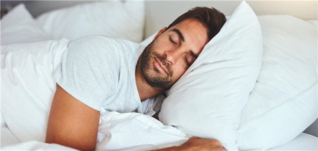 Ein Mann liegt schlafend auf zwei bequemen Kissen in einem Bett. 