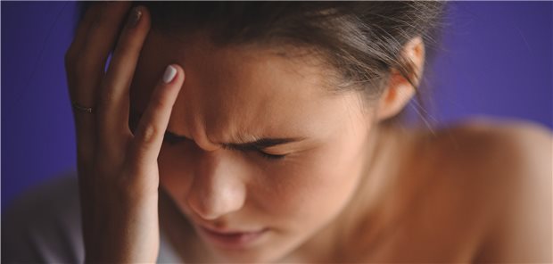 Frau, die sich mit schmerzverzerrtem Gesicht an den Kopf fasst.