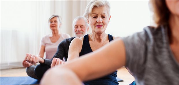 Vier ältere Personen sitzen in einem Raum im Schneidersitz und machen eine Yoga-Übung. 