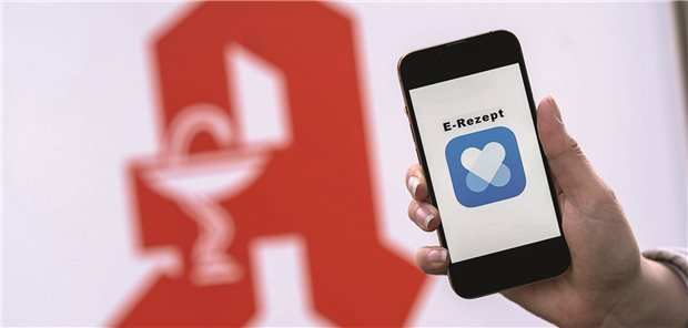 Handy mit eRezept-App-Symbol vor einem Apothekenschild
