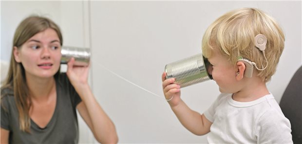 Ein Kleinkind trägt ein Cochleaimplantat und kommuniziert mit seiner Mutter über ein Dosentelefon.
