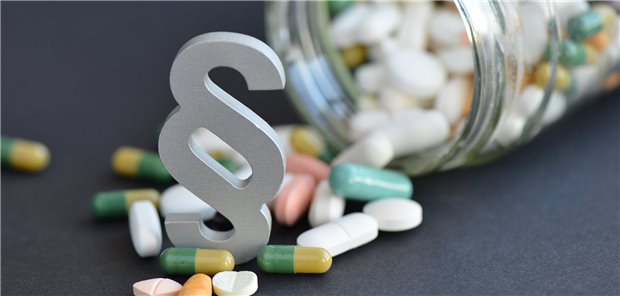 Paragraph in Tabletten, daneben ein mit Tabletten gefülltes, umgefallenes Glas.