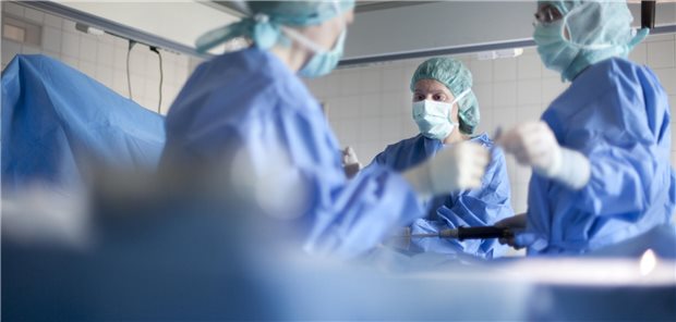 Drei Ärzte bzw Ärztinnen stehen an einem Operationstisch 