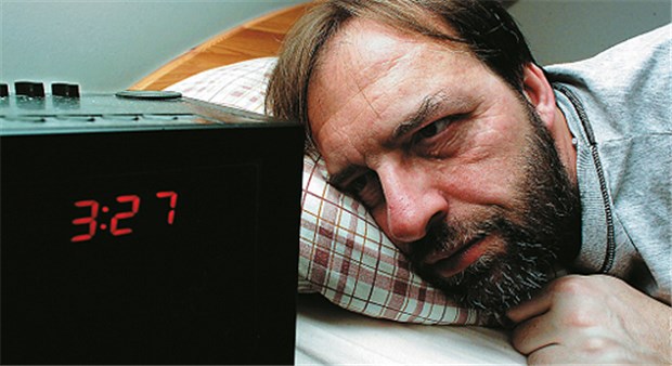 Müder Blick auf den Wecker. Insomnien können die Leistungsfähigkeit tagsüber drastisch reduzieren.