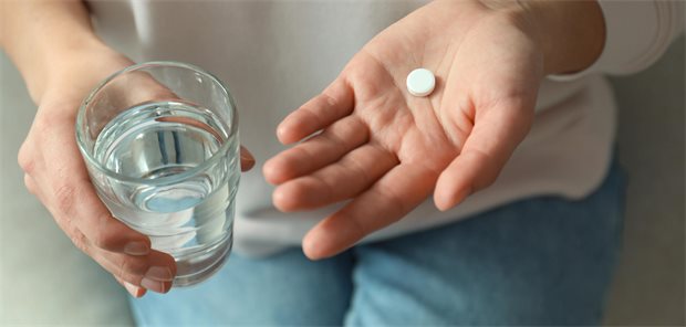 Person hält Glas Wasser in rechter Hand und weiße Tabeltte in linker Hand
