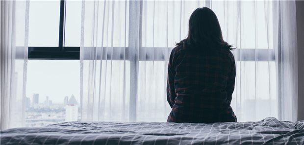 Eine Frau sitzt im dunkeln vor einem Fenster und schaut hinaus.