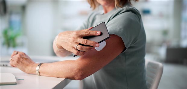 Eine Frau kontrolliert mithilfe eines kontinuierlichen Glukosemonitors regelmäßig ihre Blutzuckerwerte.