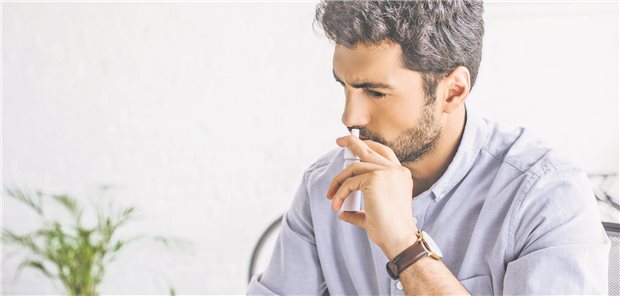 Ein Mann sprüht sich Nasenspray in die Nase