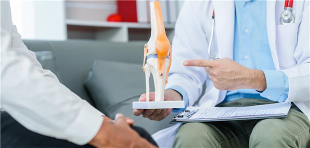 Ein Arzt bespricht den Therapieansatz mit einen Patienten mit einer chronisch-entzündlichen Gelenkerkrankung anhand eines Modells des Kniegelenkes.