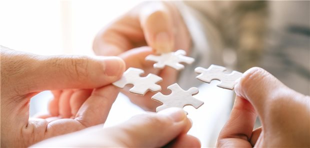 Zwei Menschen haben einzelne Puzzle-Teile in der Hand, die sie zusammenstecken wollen.