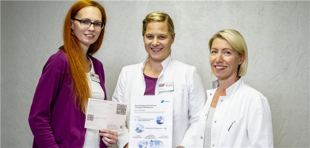 Praxismanagerin Tanja Whittington, Allgemeinärztin Annette Rennert und Diabetologin Karina Pate (v.l.n.r.) mit E-Rezept auf Papier und Aufsteller für die Information der Patientinnen und Patienten.