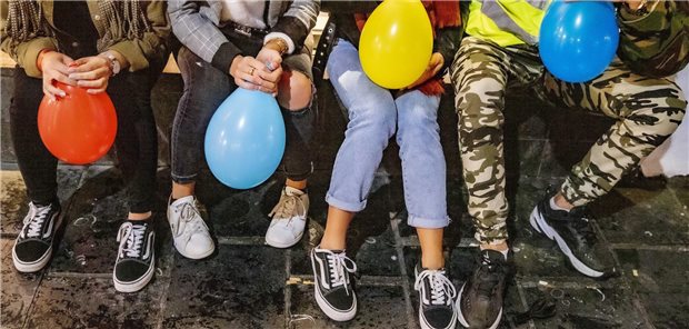 Vier Jugendliche sitzen nebeneinander auf einer Bank und halten Luftballone in der Hand, die mit Lachgas gefüllt sind.