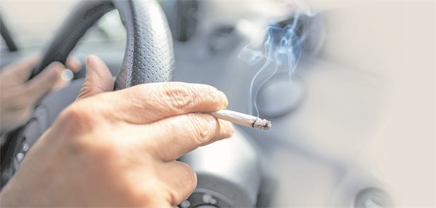 Eine Frau sitzt mit einer brennenden Zigarette hinter dem Lenkrad ihres Autos.