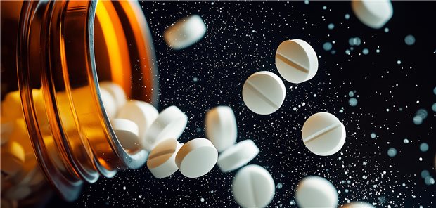 Viele weiße Tabletten fliegen aus einem braunen Glas heraus.