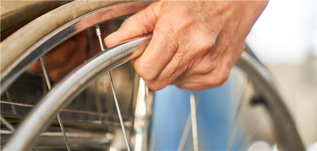 Hand eines Patienten am Reifen eines Rollstuhls.