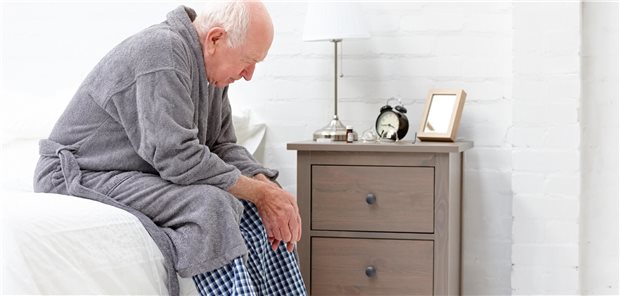 Ein Mann sitzt im Bademantel und Pyjama auf der Bettkannte. 