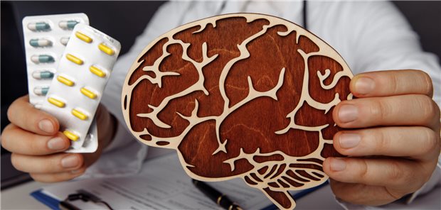 Eine Hand hält ein Gehirn-Modell in die Kamera, in der anderen Hand befinden sich zwei Medikamenten-Blister.