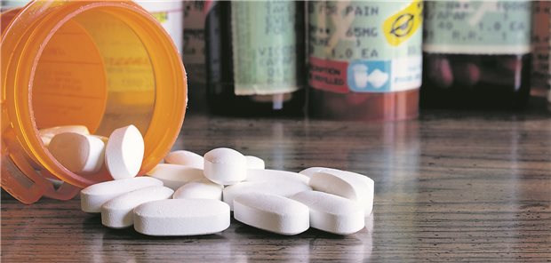 Weiße Tabletten liegen vor einer orangenen Tablettendose. Im Hintergrund stehen weitere Dosen. 